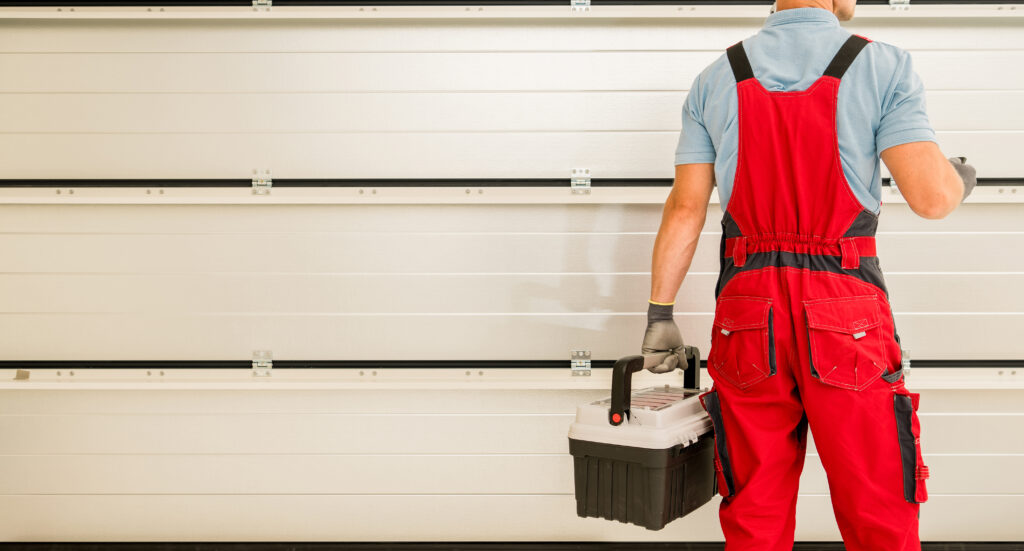 Man in red overalls holding a toolbox in front of a garage door | garage door maintenance myths

