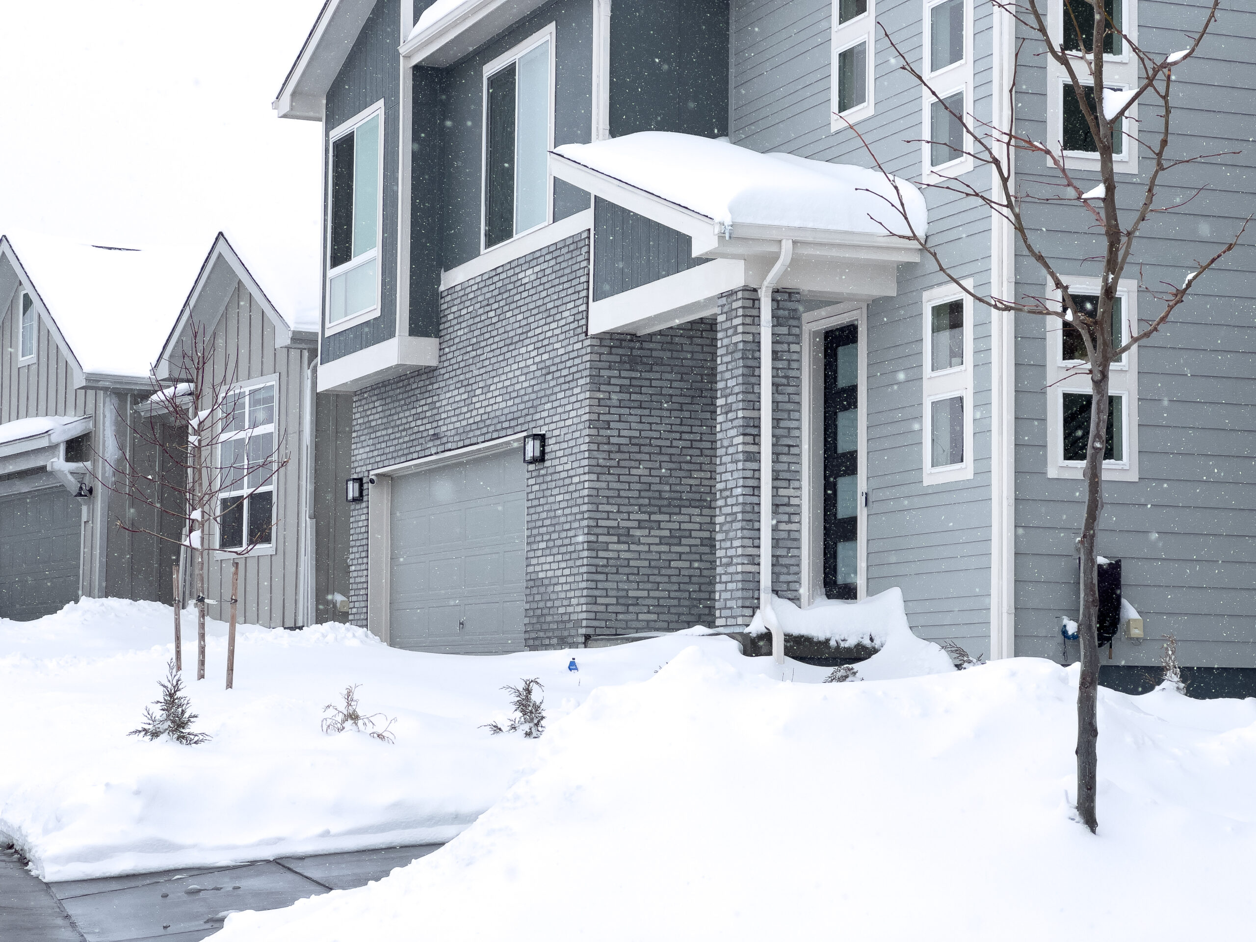 A gray condo like building covered in snow with gray garage doors
