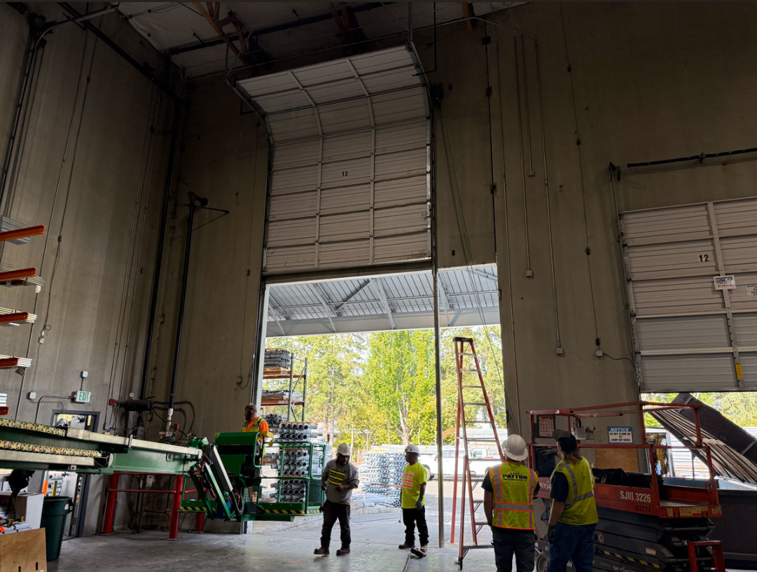 An open commercial garage door with two men around it doing repairs