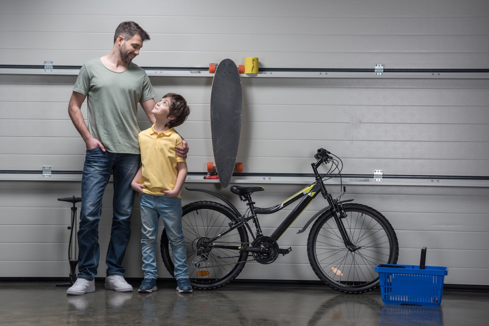 Why August Is Peak Season for Broken Springs and Garage Door Repair Dad with his arm around his son who is looking up at him in a garage